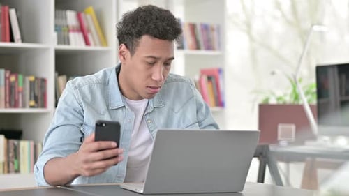 Young Adult Using Phone and Laptop at Desk