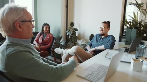 Senior Man Talking to Young Cheerful Coworkers in Office