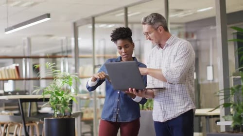 Coworkers Collaborate Using Laptop in Modern Office