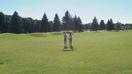 Women Holding Pride Flag in Sunny Green Park