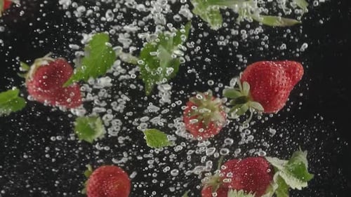 Frische Erdbeerfrüchte, die in Superzeitlupe ins Wasser fallen gelassen wurden