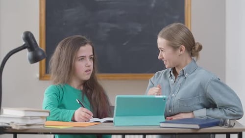 Two Young Caucasian Women Sitting at Desk in Classroom Talking Studying in University