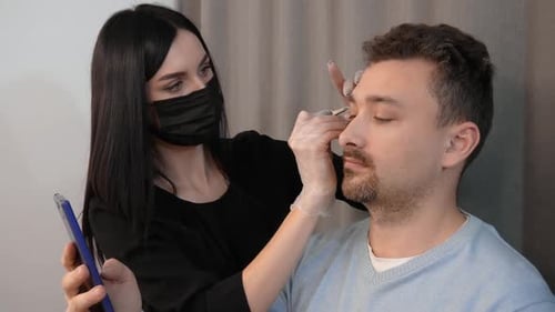 Makeup Artist Shaping Young Man's Eyebrows Indoors