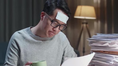 Close Up Of Sick Asian Man Drinking Water While Working Hard With Documents At The Home