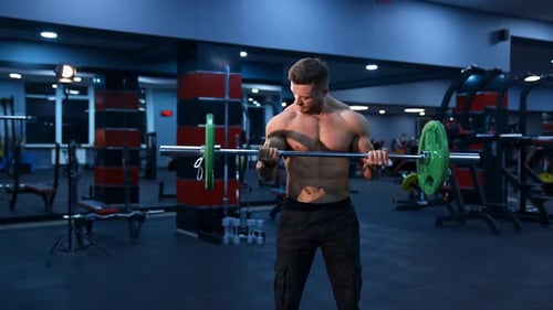 Athletic man in gym exercising with barbell. Bodybuilder with perfect body. Naked torso