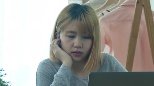 young smiling Asian woman working on laptop while at home in office work space.