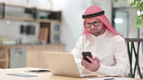 Professional Young Arab Businessman Using Smartphone and Laptop in Office