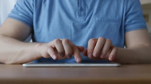 Hände eines jungen Mannes, der auf einem Tablet-PC am Tisch zu Hause tippt