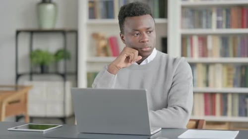 African Man Thinking While Working on Laptop in Library