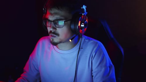 Young Man is Sitting at Computer Wearing Headphones with Headset and Talking Neon Light Front View