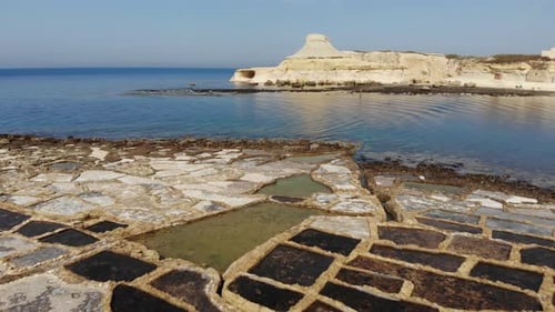 An aerial drone shot flying over the Salt Pans, rocks and crystal blue water of Gozo Island in Malta