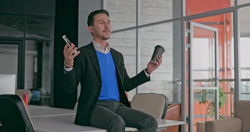 Young Serious Businessman Working in the Office Meditating in the Workplace with Closed Eyes