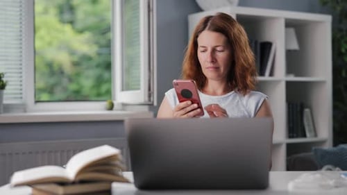 Woman Uses Smartphone in Front of Laptop