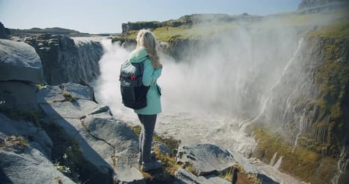Wanderin mit Rucksack blickt auf den mächtigen Detifoss-Wasserfall in Island