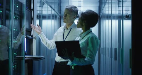 Workers in a Data Center Walking Between Rows of Server Racks