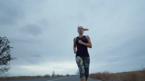 Caucasian Woman in Sportswear Trains Jogging on Road Background Cloudy Sky Low View