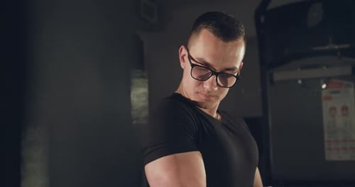 Man with Glasses Pulling Loop with Hand for Arm Muscles at Simulator in Gym