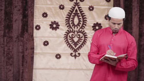 Man Writing in Book Wearing Traditional Cap
