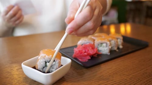 Woman Dipping Roll with Salmon in Soy Sauce While Sitting in Cafe