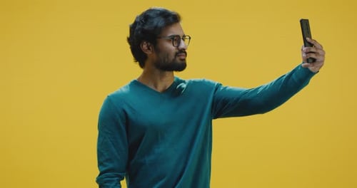 Young Adult Taking Selfie on Phone with Yellow Background