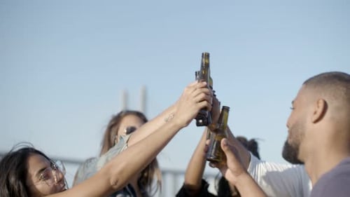 Des gens heureux qui tintent des bouteilles de bière contre le ciel bleu.