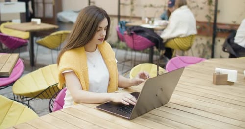 Woman Works on Laptop at Cafe with Drink