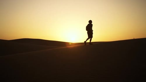 Silhouette Of Man Walking Along Sand Dunes