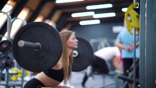 Woman bodybuilder approaching barbell and squatting with it