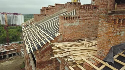 Aerial view of unfinished brick apartment building with wooden roof structure under construction.