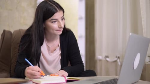 Woman Studying and Writing at a Laptop