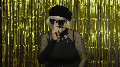 Ältere alte Frau mit stilvoller Sonnenbrille, zeigt mit dem Finger auf die Kamera, sieht glücklich aus, Person aussuchen