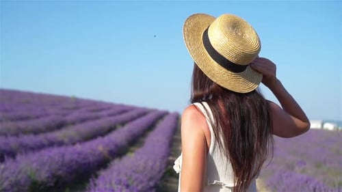 Femme dans un champ de fleurs de lavande au coucher du soleil en robe blanche et chapeau