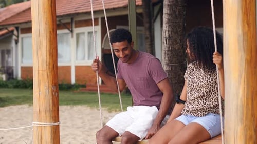 Romantic Young African Couple Swinging on a Beach Swing Smiling and Talking