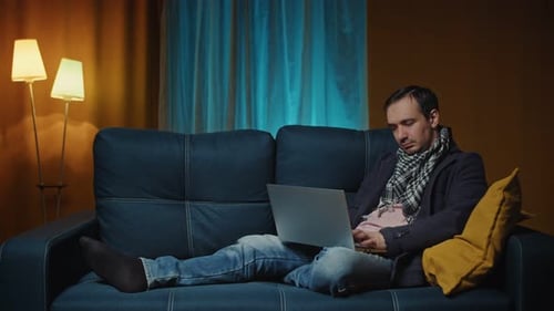 Man Napping on Couch While Using Laptop