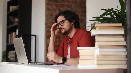 Stylish man sitting at table in home office and using laptop
