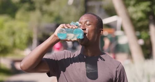 Tired but Happy African American Sportsman Drinking Water After Intense Workout in Urban Park