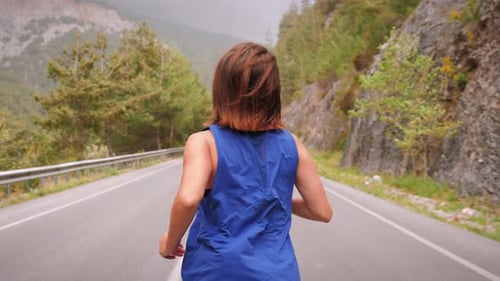 Back follow shot of female marathon runner exercising on empty mountain road