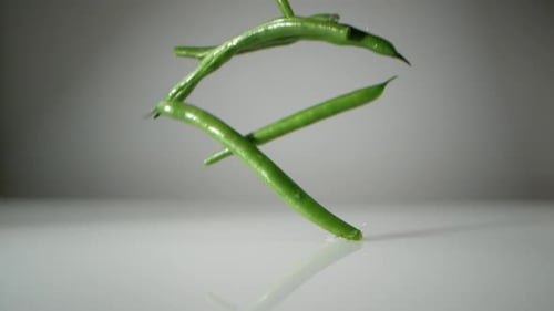 Grüne Bohnen auf der Wasseroberfläche. Zeitlupe.