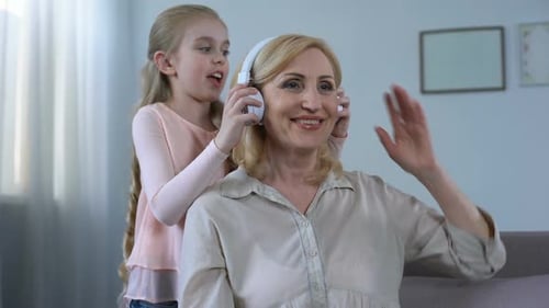 Girl Puts Headphones on Smiling Woman in Living Room