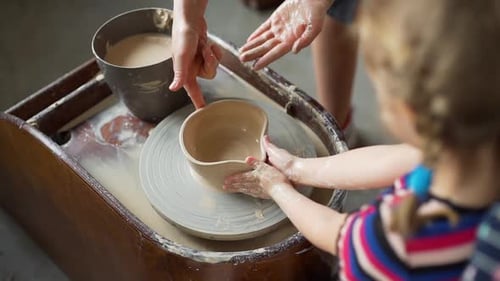 Child and Adult Shaping Clay on Pottery Wheel
