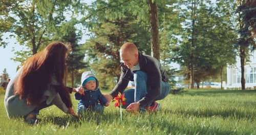 Happy Little Kid is Playing with His Parents in the Park on the Grass in the Sunlight