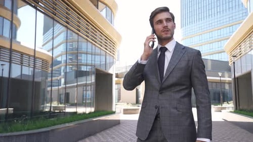 Young Businessman in a Suit Standing Near a Glass Skyscraper and Talking on a Mobile Phone, Top