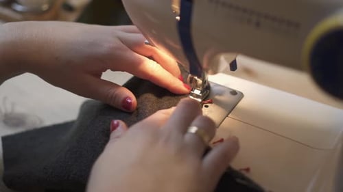 Close up of cropped female hands sewing fabric on professional manufacturing machine