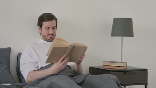 Young Man Reading Book While Sitting in Bed