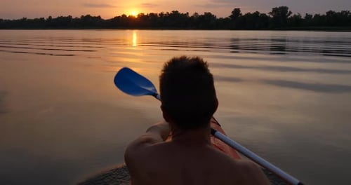 A Man Kayaks on a Calm River Towards the Sunset
