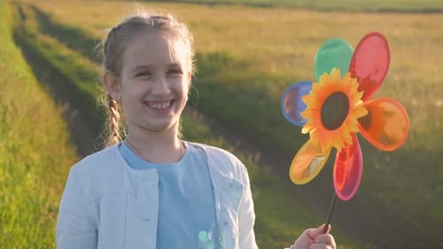 Happy Girl Holding Wind Toy in Green Field, Rejoicing Life. Cheerful Child in the Meadow with Wind