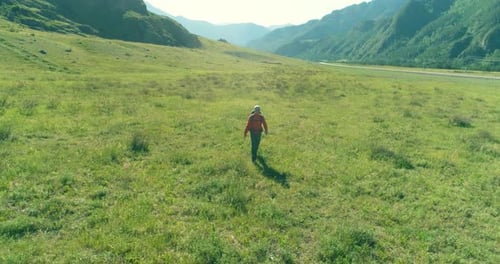 Flight Over Backpack Hiking Tourist Walking Across Green Mountain Field. Huge Rural Valley at Summer