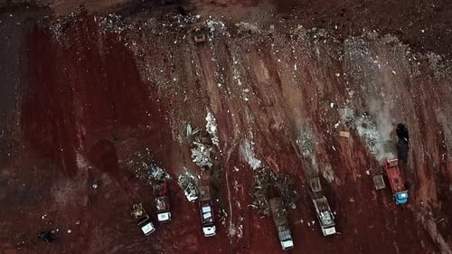 Dump trucks unload heaps of garbage as bulldozers push the piles into the landfill - aerial view