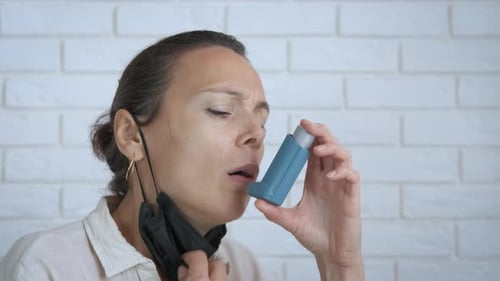 Woman Using Inhaler with Face Mask Around Neck