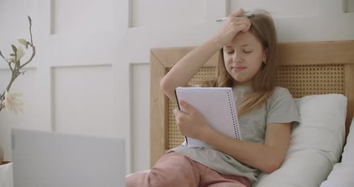 Online-Bildung für Schulkinder, Mädchen lernt von zu Hause aus, Sitzen auf dem Bett mit Laptop, Halten